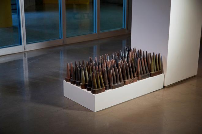 Ceramic installation in gallery featuring a grouping of spike shaped tiles placed low to the ground. 